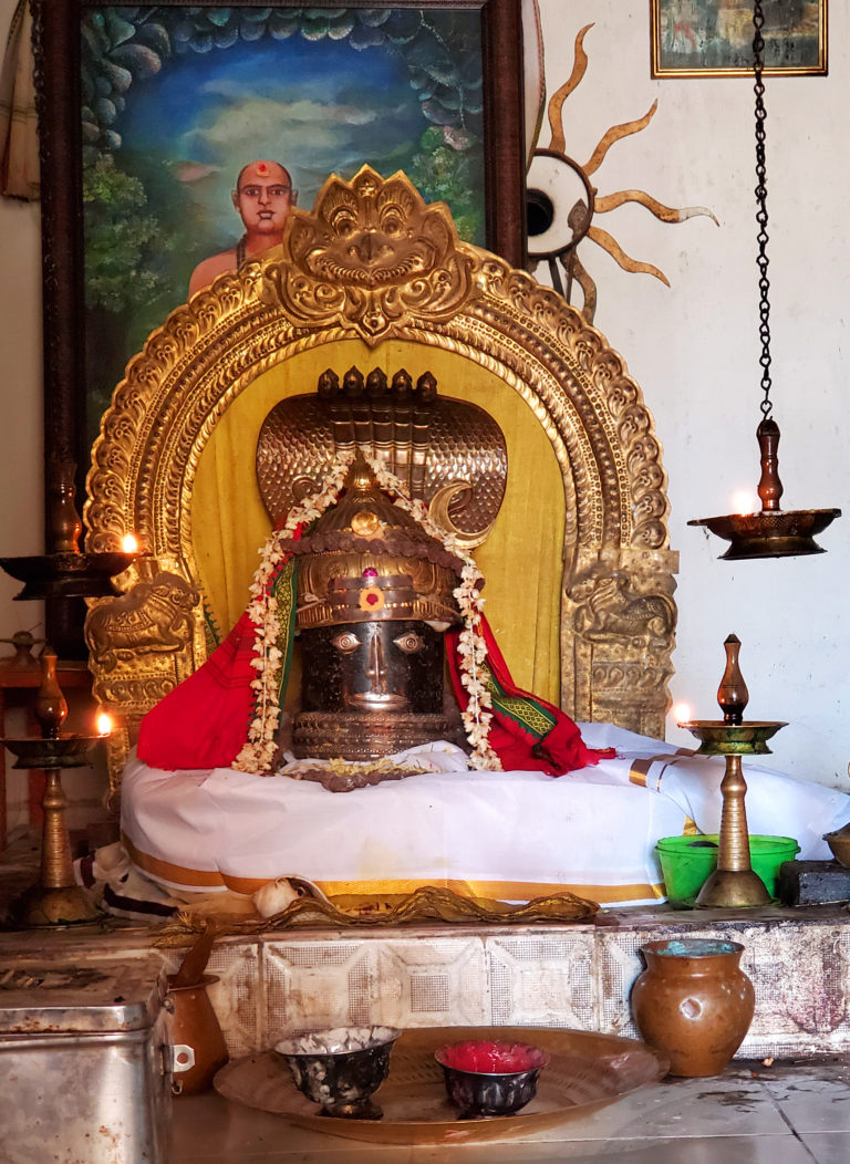 A photograph of a black phallic stone, upon which is engraved a face, set in a gold frame and lit by lamps
